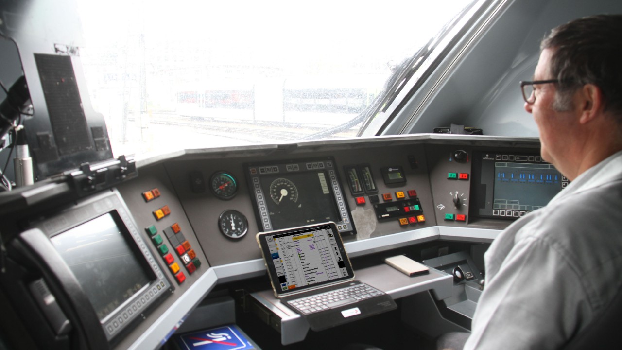 Un mécanicien de locomotive assis dans la cabine de conduite d’un train ICN regardant l’affichage de la ponctualité sur sa tablette.