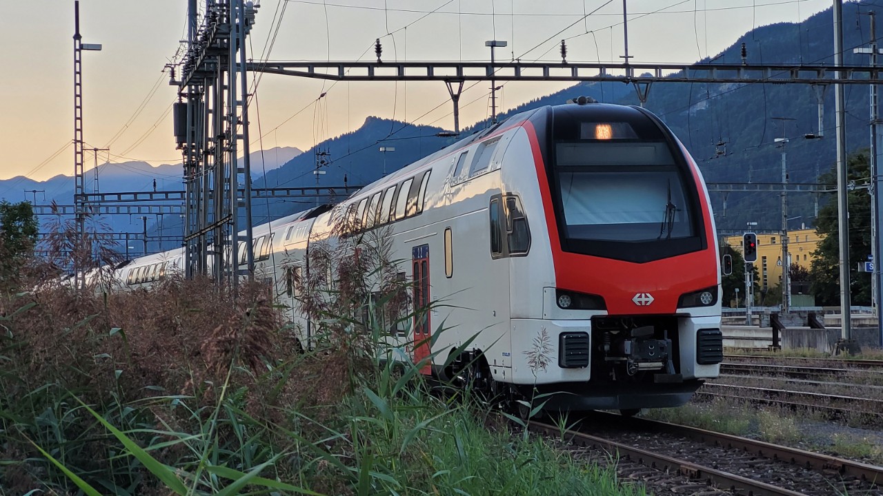 Un train Duplex IR est garé sur un faisceau de voies, avec en arrière-plan le soleil qui se couche derrière la montagne.
