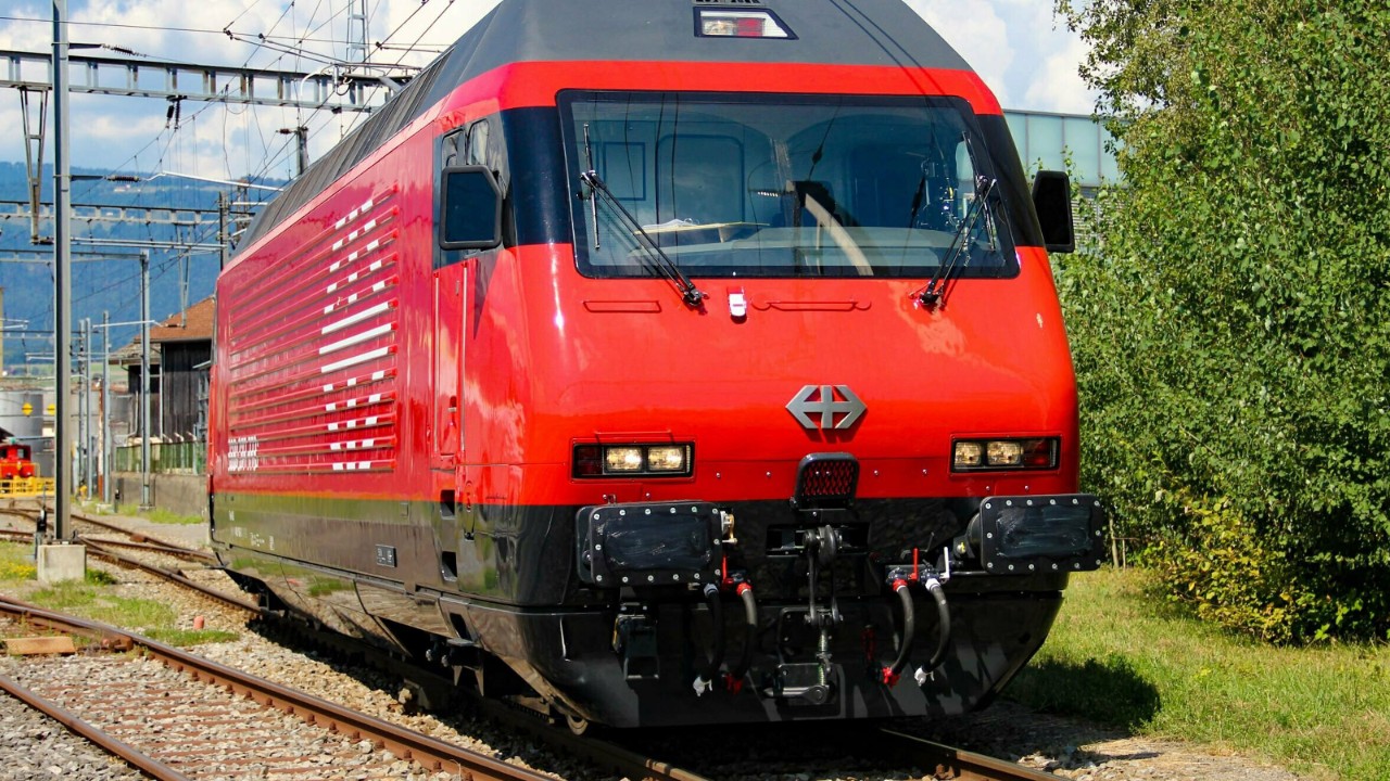La photo montre une locomotive rouge de type Re 460 devant un atelier.