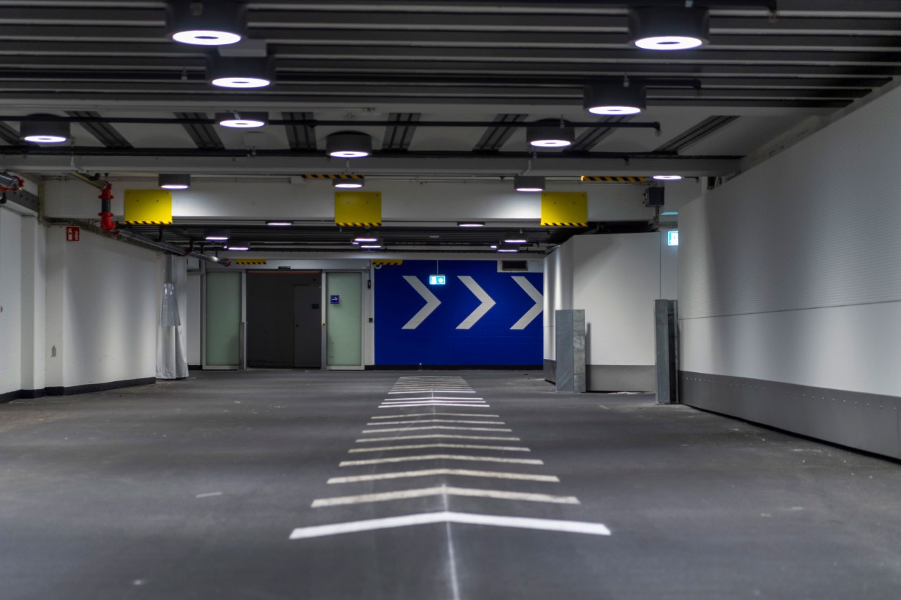 Das Foto zeigt die Unterführung Richtung Ausgang gesehen. Markant sind die Bodenmarkierungen mittels weissen Pfeilen und blaue Wand beim Ausgang mit ihren weissen Pfeilen.